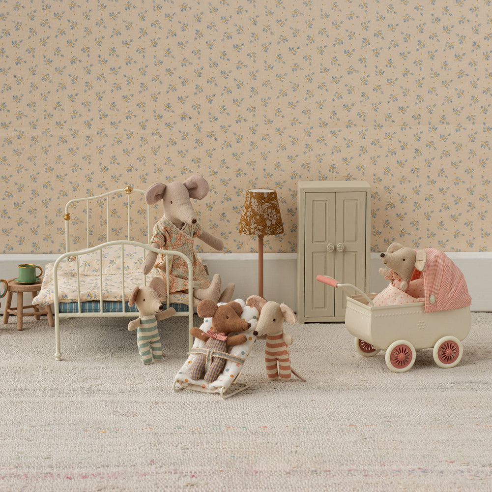 Miniature bedroom scene with toy furniture and animals in a room with floral wallpaper.