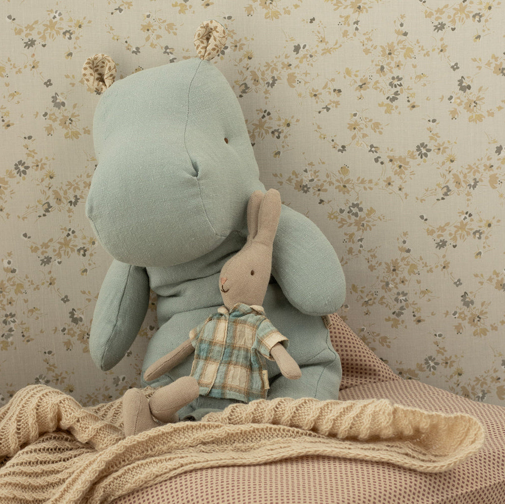 Large plush rabbit holding a smaller plush bear with a checkered shirt against a floral wallpaper background.