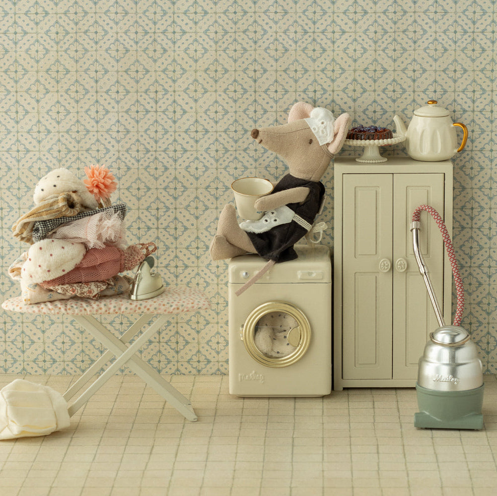 Miniature scene with a mouse on a washing machine, teapot, and vacuum cleaner against a patterned wall.