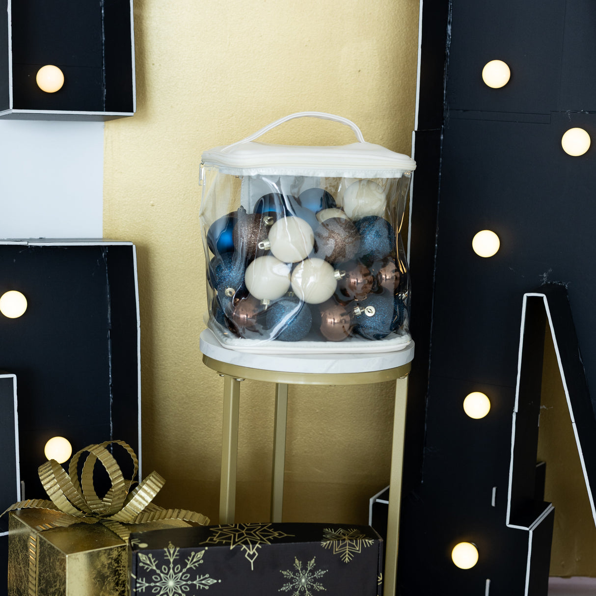 Decorative setup with a clear container of ornaments, gold gift box, and black letter decorations.