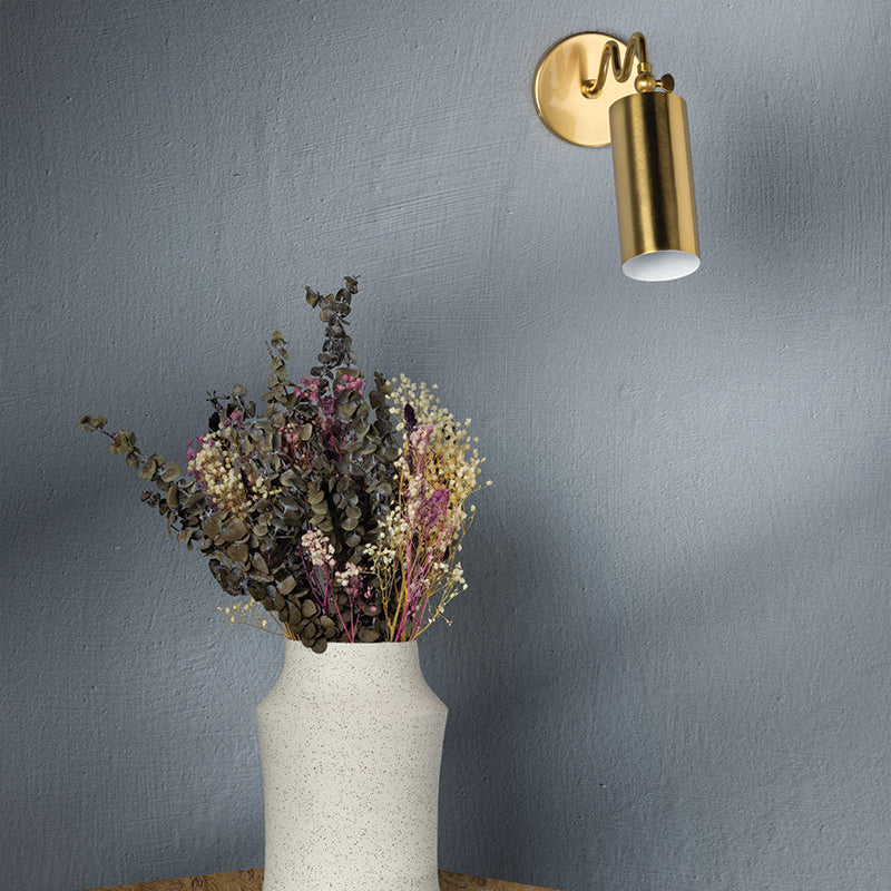 Gold wall-mounted light fixture next to a vase with dried flowers on a textured surface.