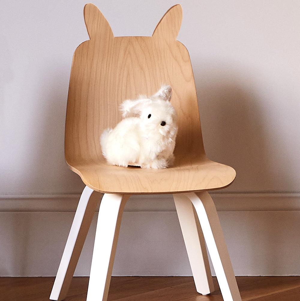 Wooden chair with bunny ears and a white fluffy toy on a wooden floor.