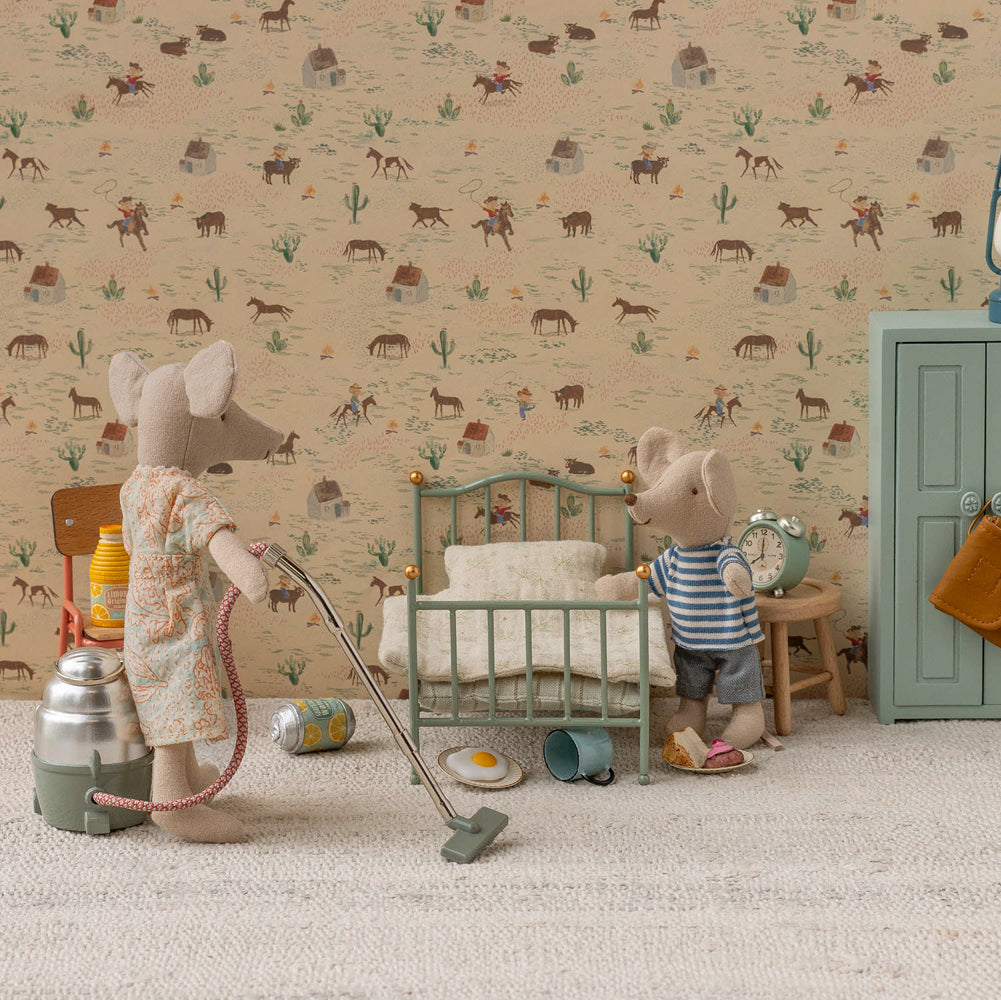 Miniature scene with toy mice in a room setting, including a bed and dresser, with a patterned wallpaper background.