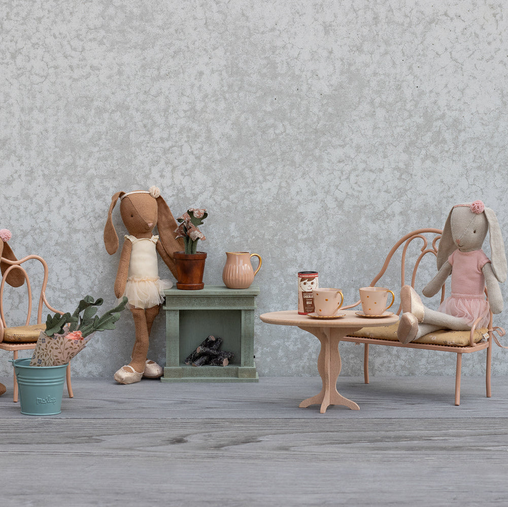 Miniature dollhouse scene with rabbits and furniture against a textured wall.