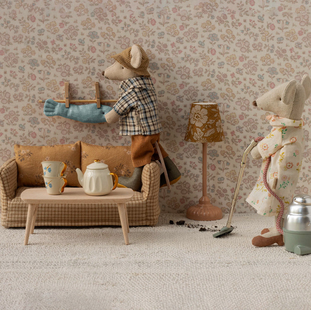 Miniature living room scene with toy mice and furniture against a floral wallpapered wall.
