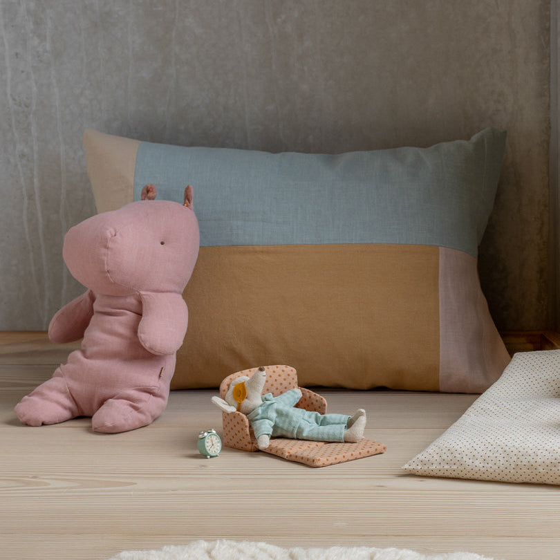Children's toys including a pink hippo, brown bunny, and green teddy bear on a wooden surface with pillows in the background.