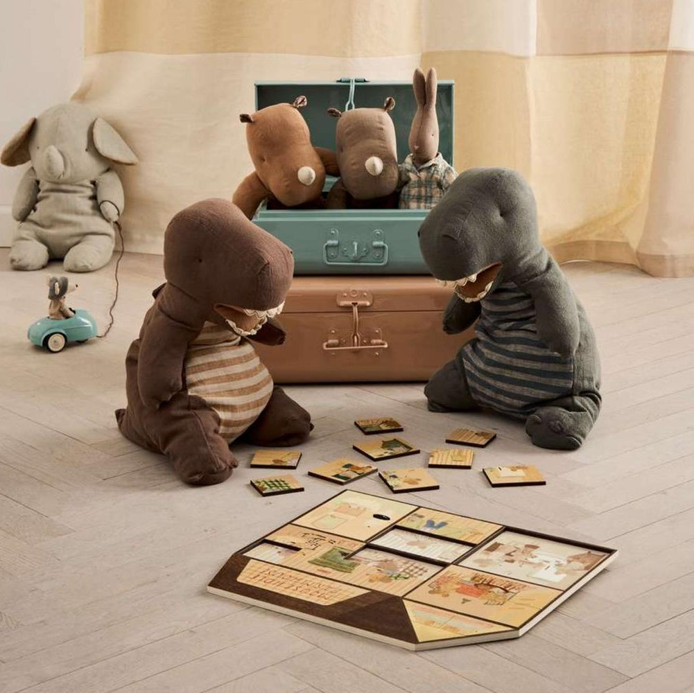 Stuffed animal toys playing with a suitcase and cards on a wooden floor.