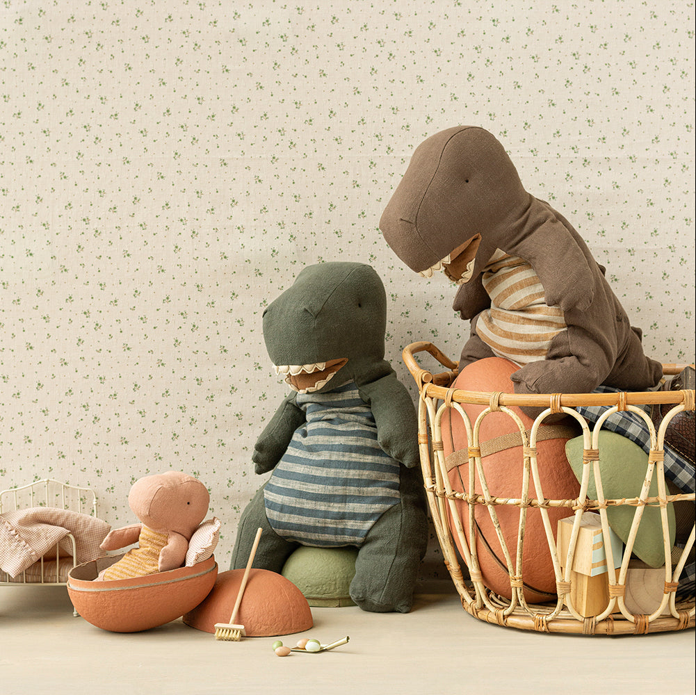 Children's toys, including a dinosaur and teddy bear, in a basket against a floral-patterned wall.