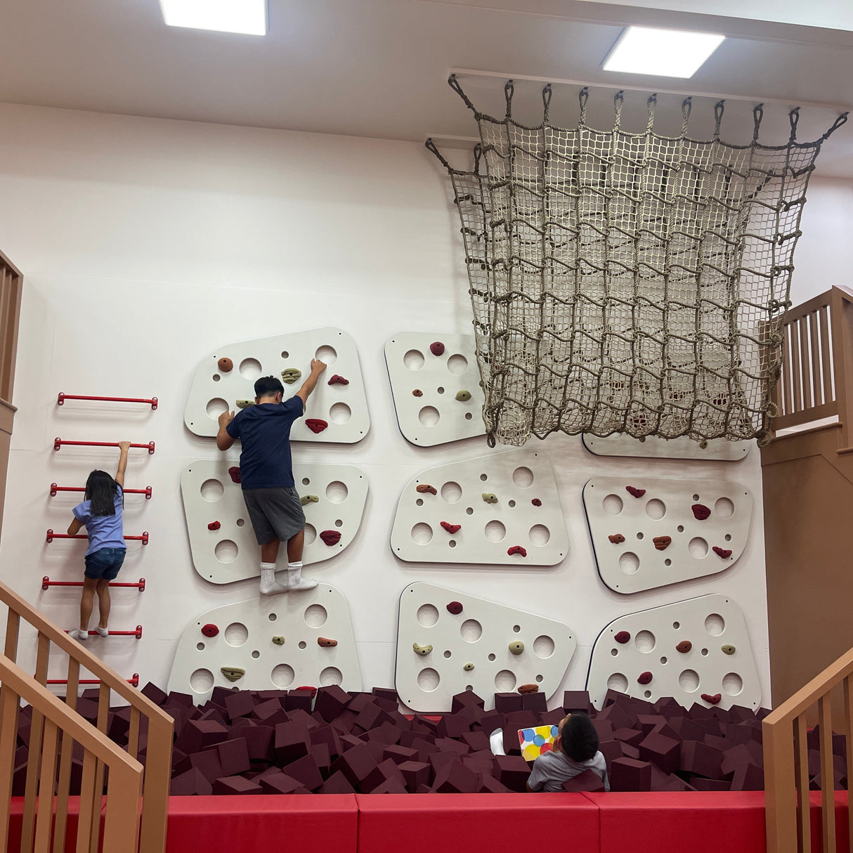 Children playing on an indoor climbing wall with a net above.