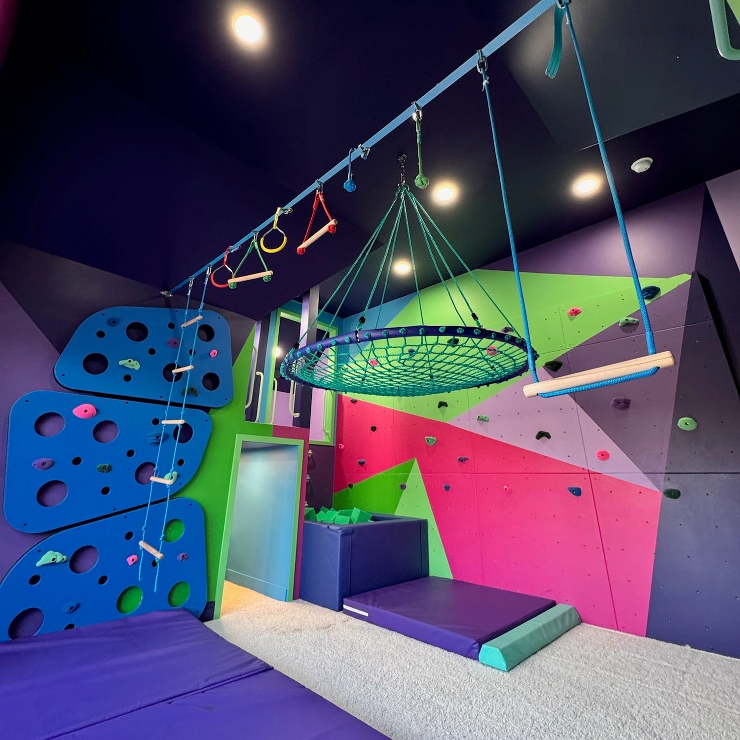 Children's indoor play area with colorful swing, and foam mats.
