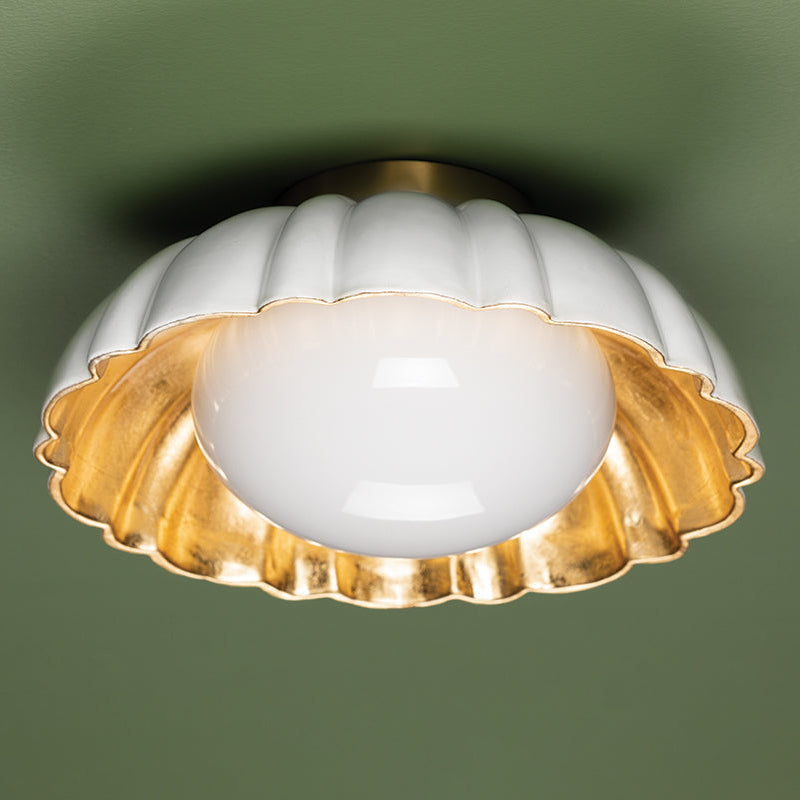 Decorative ceiling light fixture with white glass shade and gold metal trim on a green background