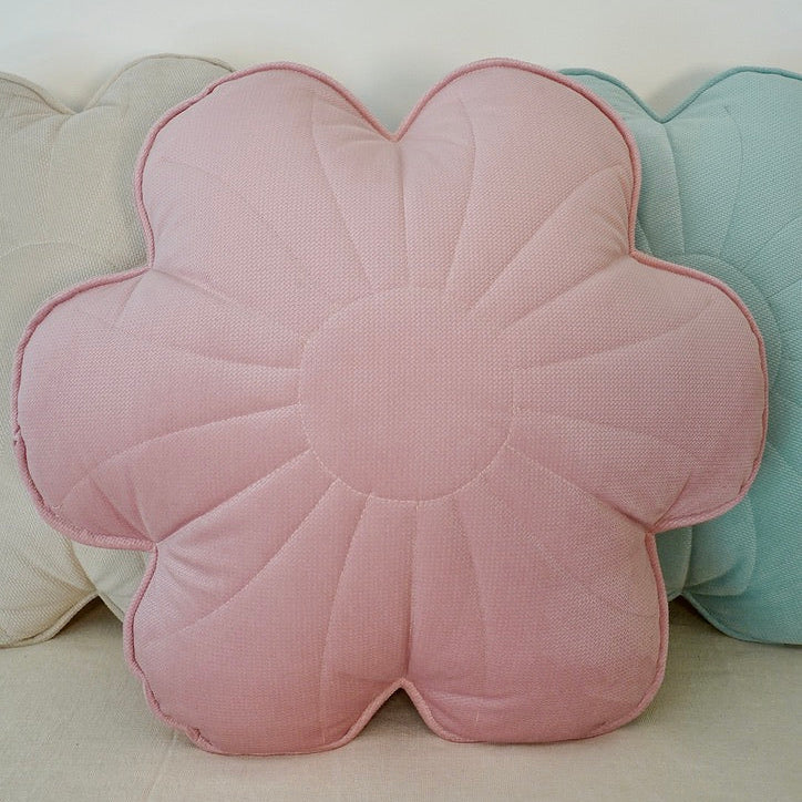 Floral-shaped pink cushion among other colorful cushions on a light background