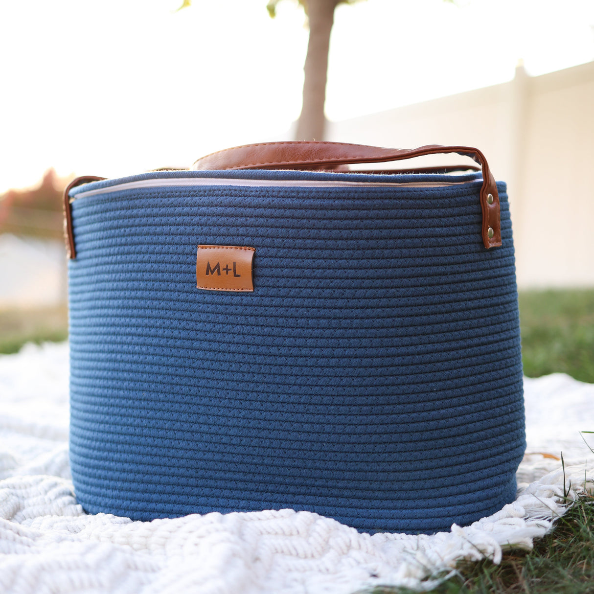 Blue woven basket with leather handle on a white blanket outdoors