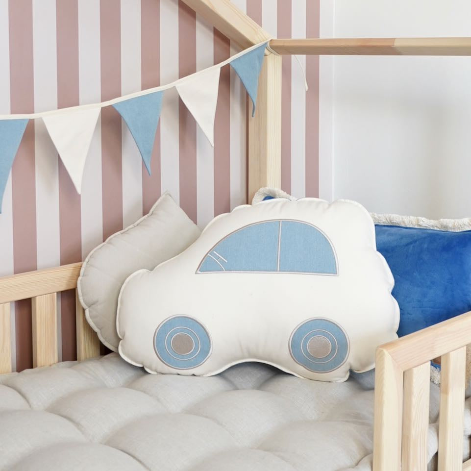 Car-shaped pillow in a crib with striped wall and flag banner