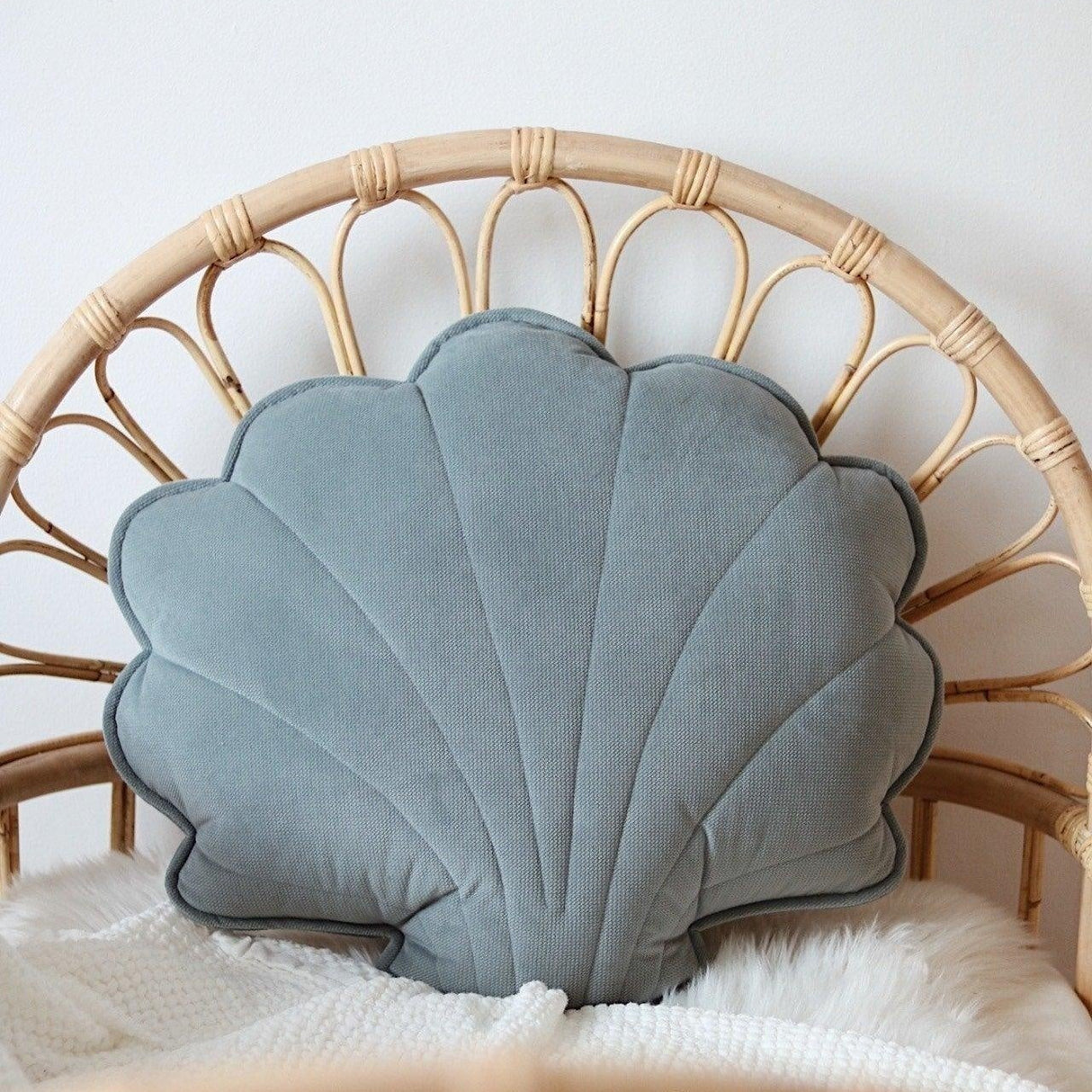 Shell-shaped blue pillow on a wicker chair with a white blanket