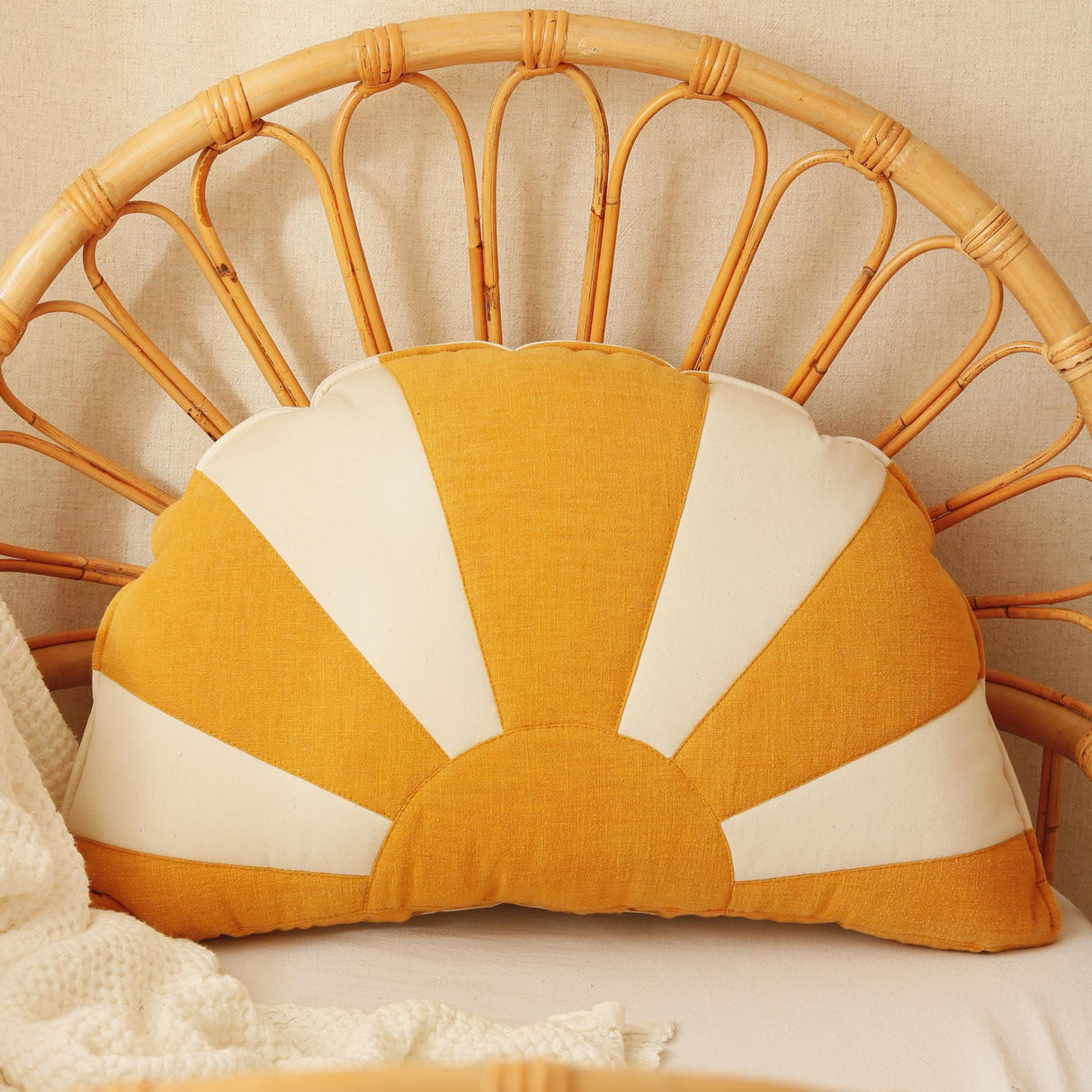 Sun-shaped pillow with yellow and white design on a wicker chair.