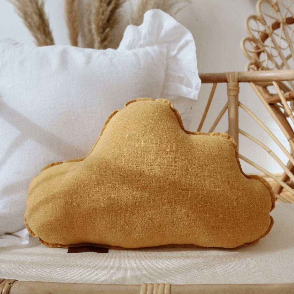Yellow cloud-shaped pillow on a wicker surface with white pillows and decorative elements in the background.