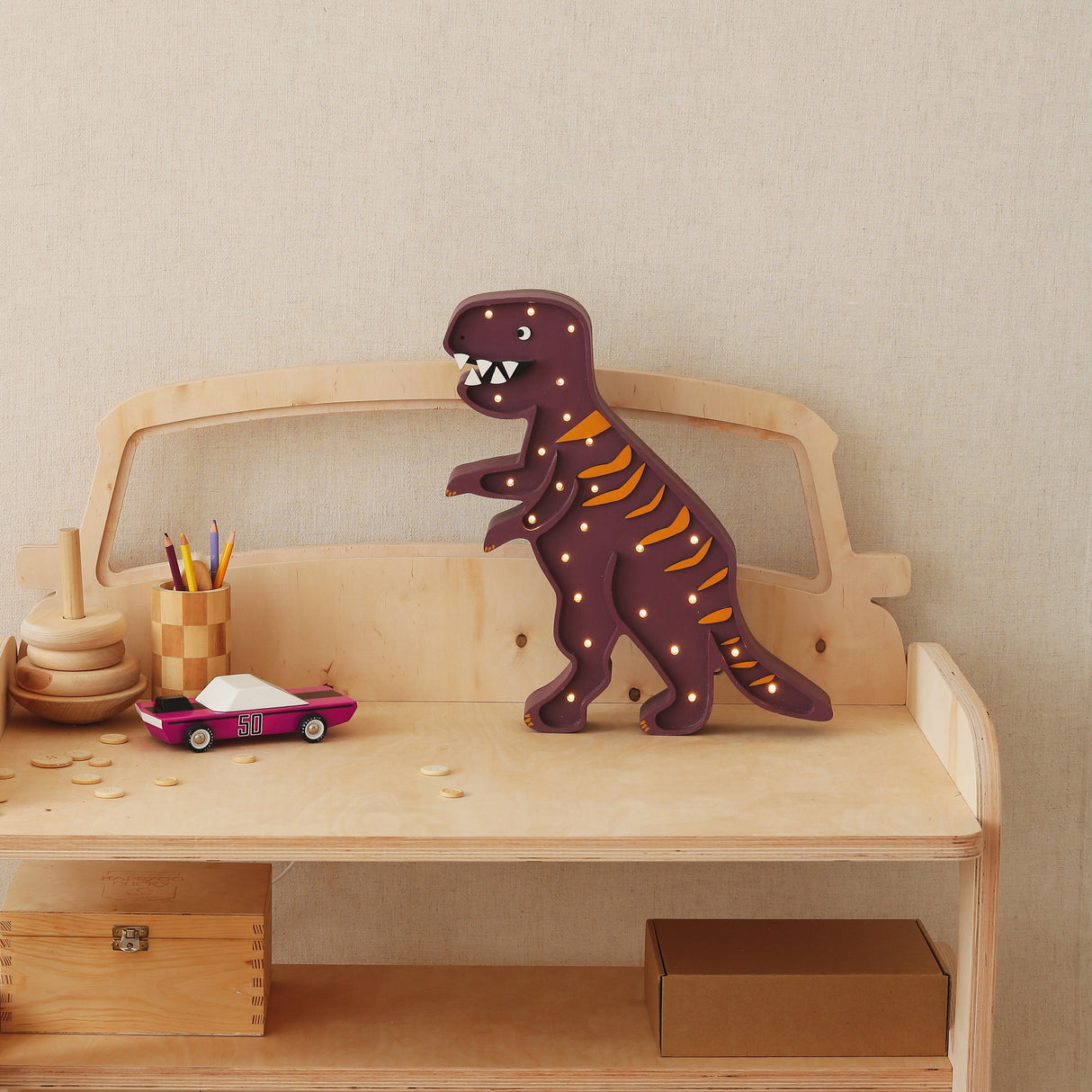 Wooden toy car with a dinosaur figure on top against a plain wall.