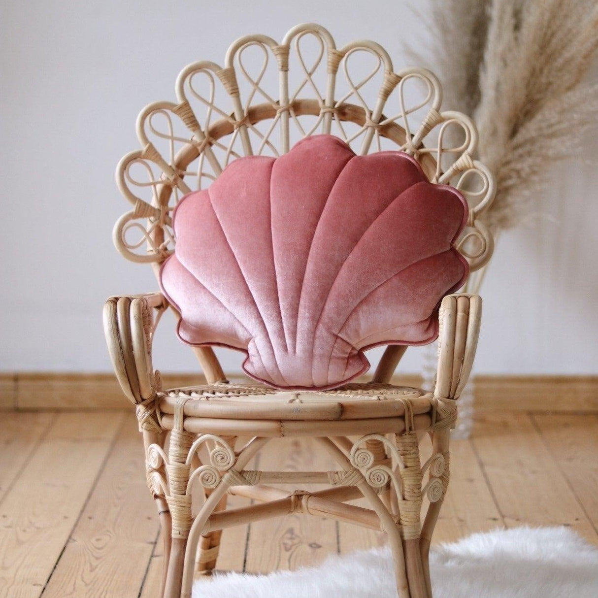 Wicker chair with a pink shell-shaped pillow on a wooden floor.
