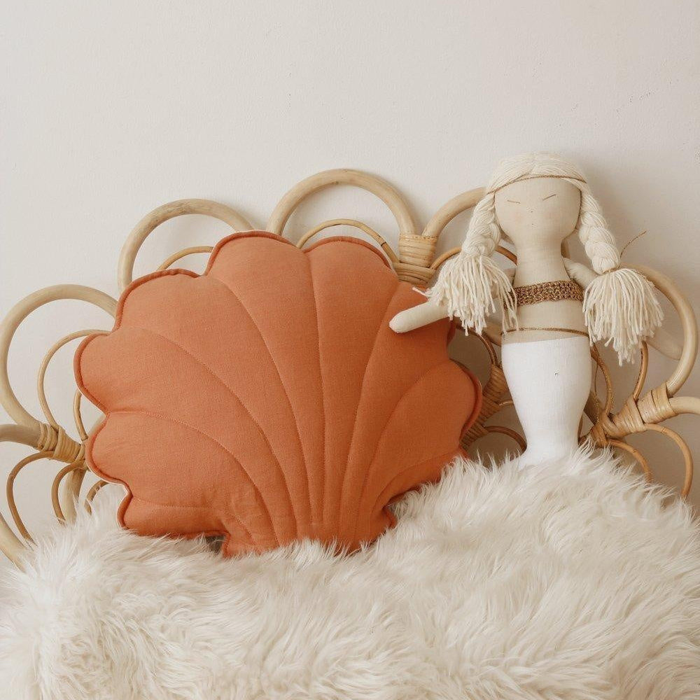 Shell-shaped pillow and doll on a fluffy surface with a neutral background