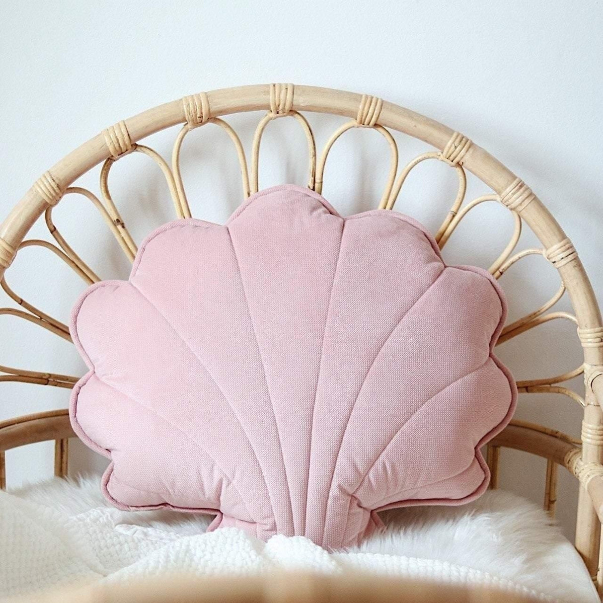 Pink shell-shaped pillow on a wicker chair with a white blanket