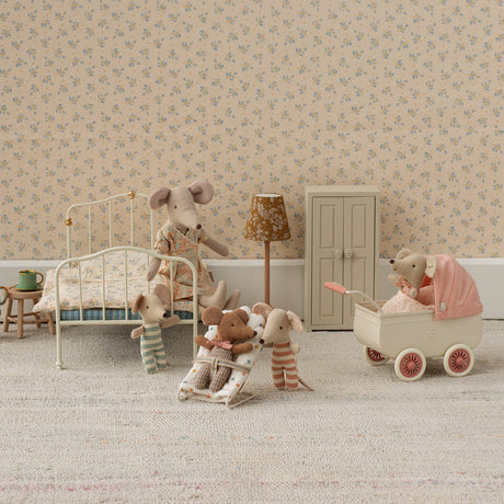 Miniature bedroom scene with toy furniture and animals in a room with floral wallpaper.