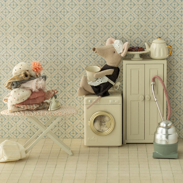 Miniature scene with a mouse on a washing machine, teapot, and vacuum cleaner against a patterned wall.