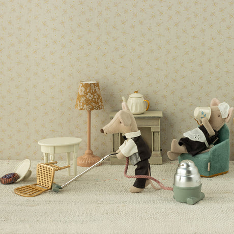 Miniature scene with toy mice in a room setting, one cleaning with a broom and dustpan, the other sitting in a chair.