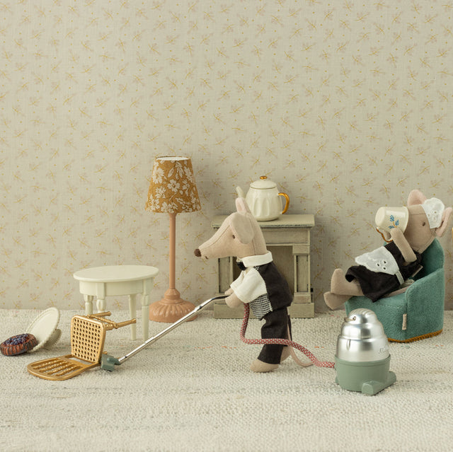 Miniature scene with toy mice in a room setting, one cleaning with a broom and dustpan, the other sitting in a chair.