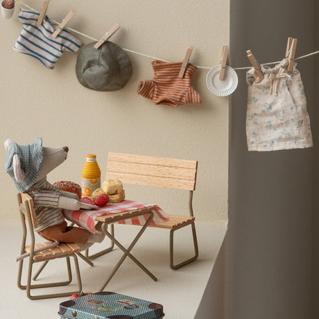 Children's play area with wooden chairs, table, and toys against a neutral wall with hanging clothes.