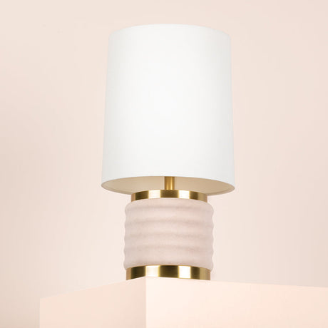 Wall-mounted lamp with white shade and gold base on a beige background