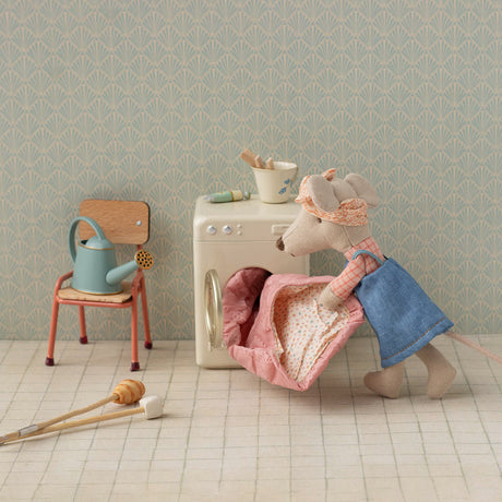 Small toy mouse in a kitchen setting with a chair, washing machine, and utensils.