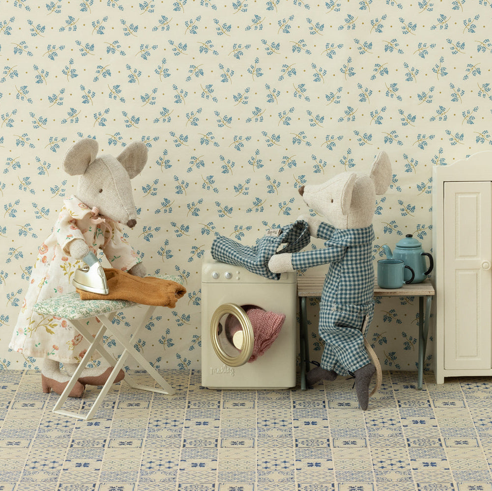 Two teddy bears in a room with floral wallpaper and a washing machine.