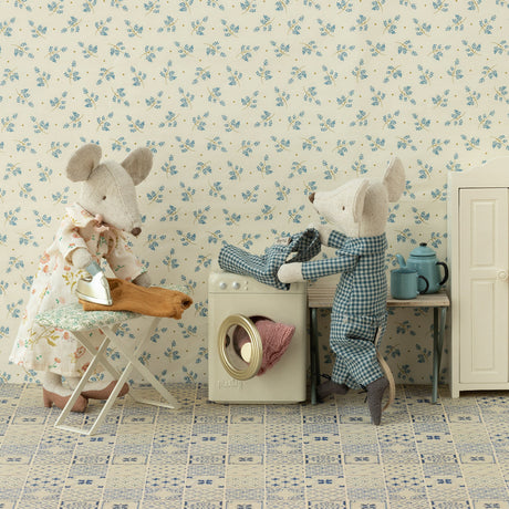 Two teddy bears in a room with floral wallpaper and a washing machine.