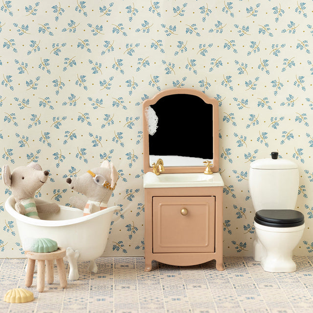 Miniature bathroom set with sink, toilet, and bathtub against a floral wallpapered wall.