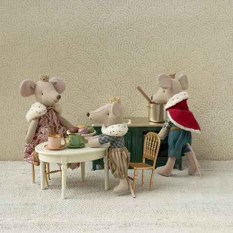 Miniature mouse figures in a tea party scene with a decorative wall background.