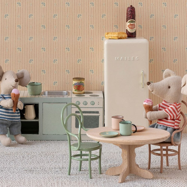 Miniature kitchen scene with toy mice, refrigerator, and furniture against a patterned wall.
