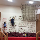 Children playing on an indoor climbing wall with a net above.