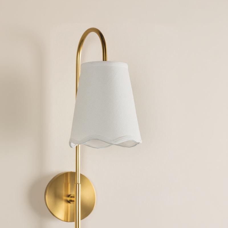 Wall-mounted lamp with gold fixture and white shade on a beige background