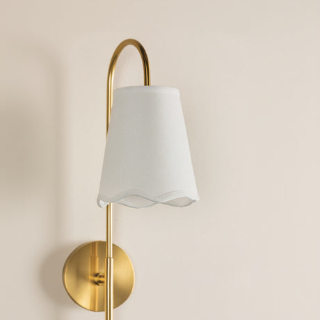 Wall-mounted lamp with gold fixture and white shade on a beige background