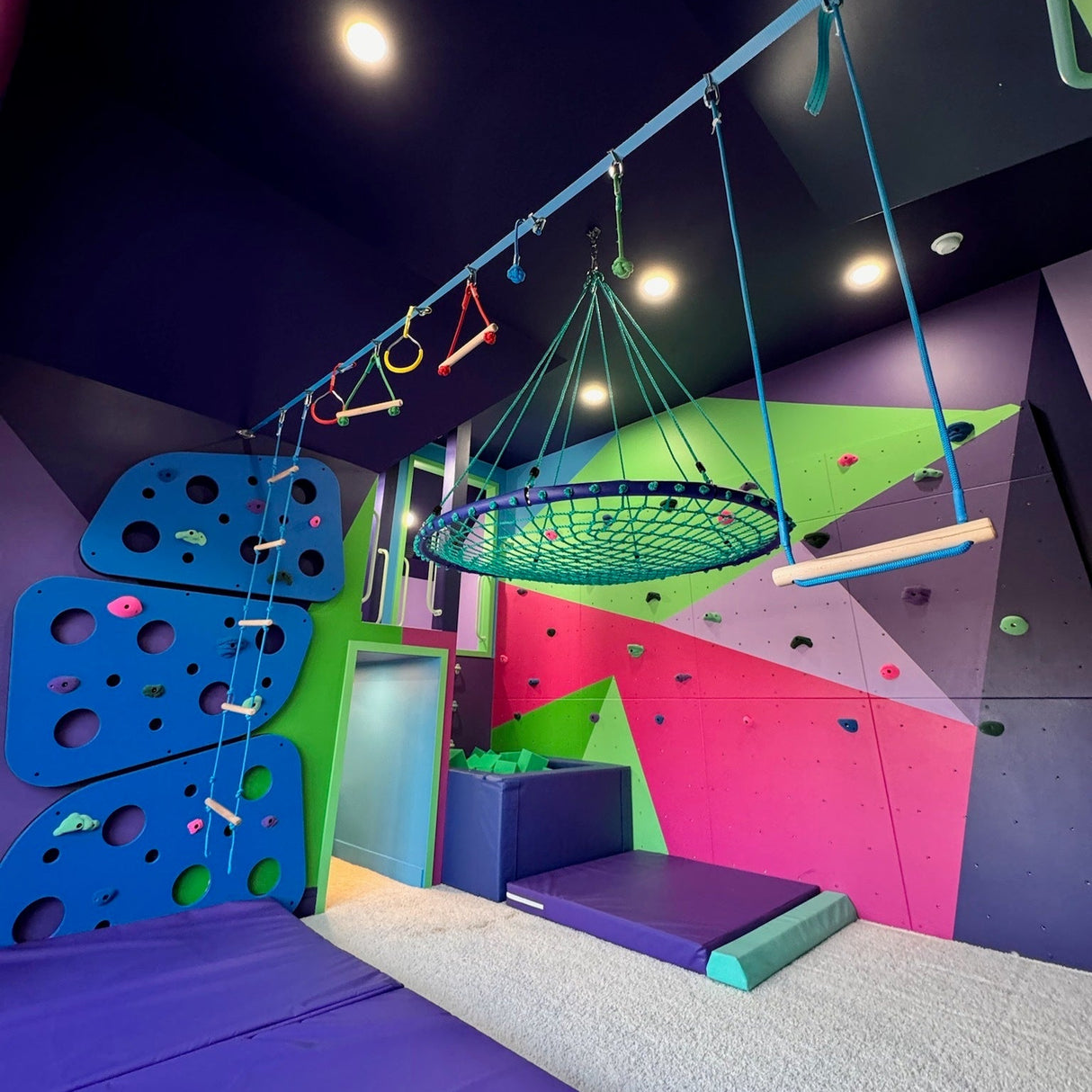 Children's indoor play area with colorful swing, and foam mats.