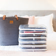 Stack of clear storage containers on a bed next to a gray basket