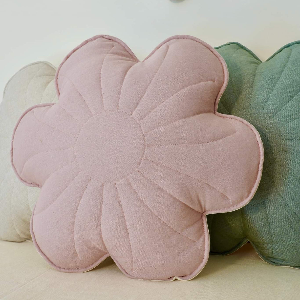 Floral-shaped pink cushion on a bed with decorative pillows and a flower banner in the background.