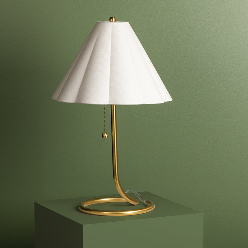 Table lamp with white shade and gold base on a green pedestal against a green background