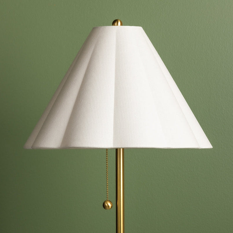 Floor lamp with a white shade and gold base against a green wall