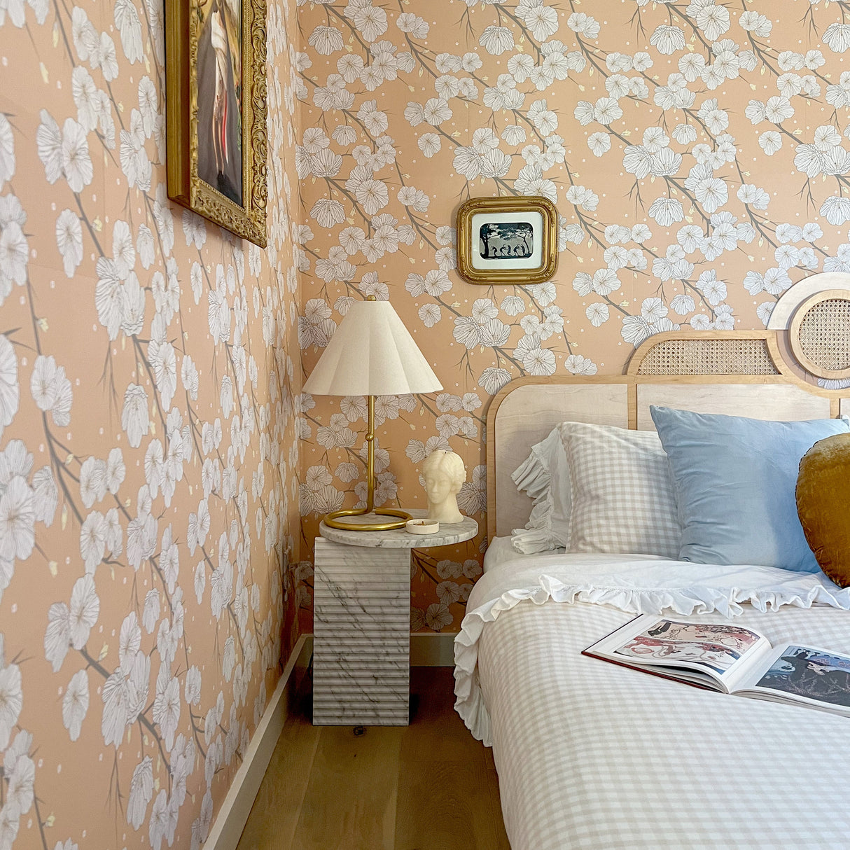 Bedroom with floral wallpaper, bed, lamp, and framed pictures.