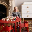 Child playing with building blocks at a red table in a room with a fireplace and white dresser.