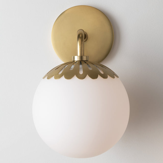 Wall-mounted light fixture with gold decorative shade and white glass on a plain background