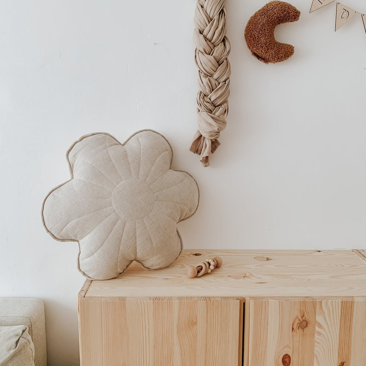 Flower-shaped cushion on a wooden dresser with decorative items on a white wall.