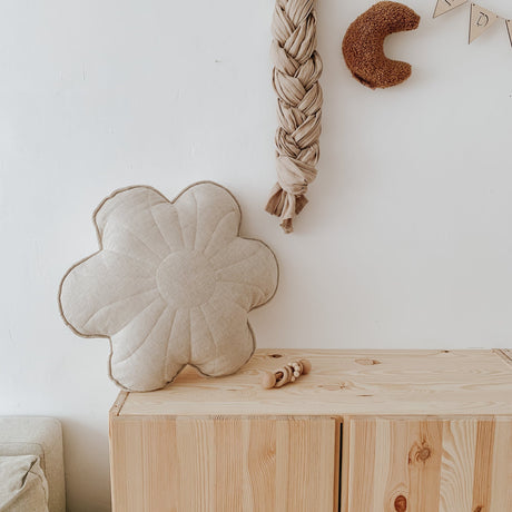 Flower-shaped cushion on a wooden dresser with decorative items on a white wall.